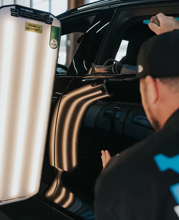 Mitarbeiter kontrolliert Karosserie eines Autos